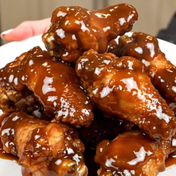 A close-up of sticky maple bacon chicken wings piled on a white plate.