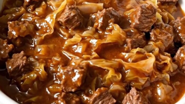 A slow cooker filled with layers of ground beef, chopped cabbage, and tomato sauce before cooking.