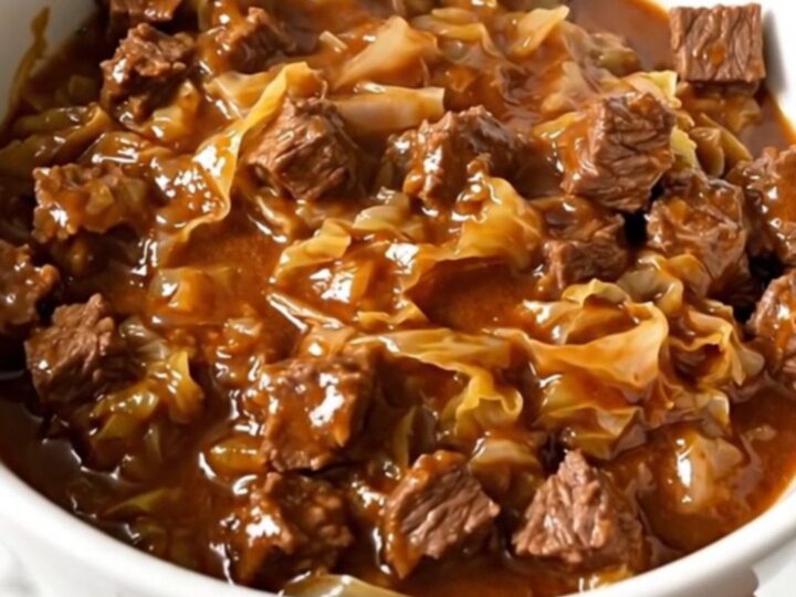 A slow cooker filled with layers of ground beef, chopped cabbage, and tomato sauce before cooking.