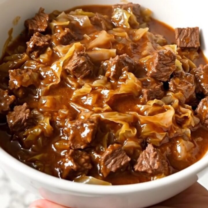 A slow cooker filled with layers of ground beef, chopped cabbage, and tomato sauce before cooking.