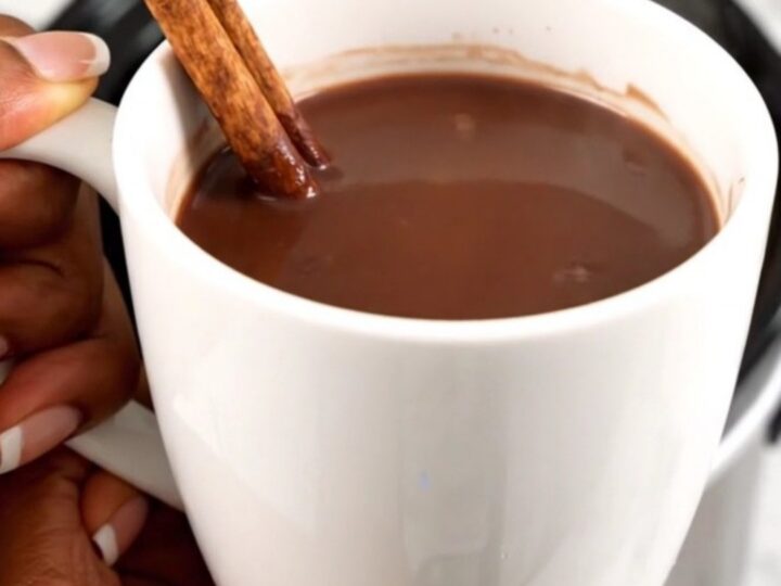 A white mug filled with rich, glossy Mexican hot chocolate, garnished with a cinnamon stick