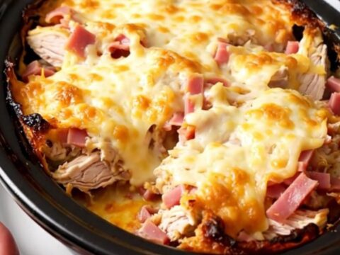 A creamy slow cooker chicken cordon bleu casserole topped with melted Swiss cheese in a black pot.