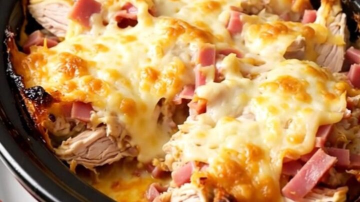 A creamy slow cooker chicken cordon bleu casserole topped with melted Swiss cheese in a black pot.