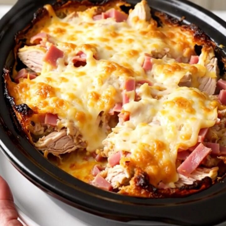 A creamy slow cooker chicken cordon bleu casserole topped with melted Swiss cheese in a black pot.