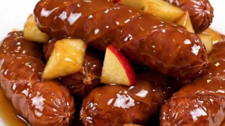 A close-up of sliced kielbasa and tender apple chunks coated in a glossy, dark cider glaze on a white plate.