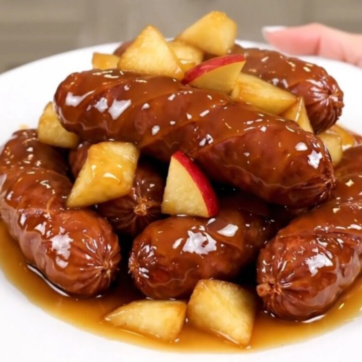 A close-up of sliced kielbasa and tender apple chunks coated in a glossy, dark cider glaze on a white plate.