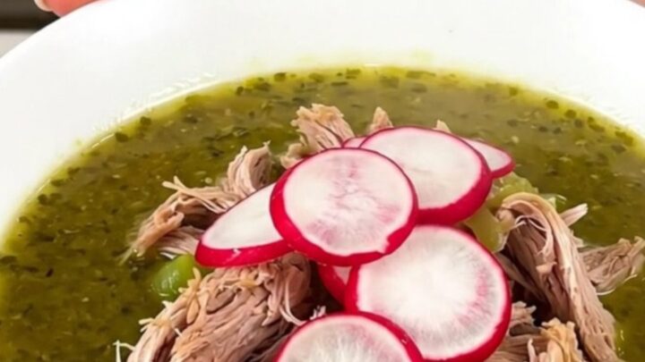 A steaming white bowl filled with shredded pork pozole verde, topped with fresh radish slices.