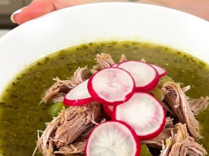 A steaming white bowl filled with shredded pork pozole verde, topped with fresh radish slices.