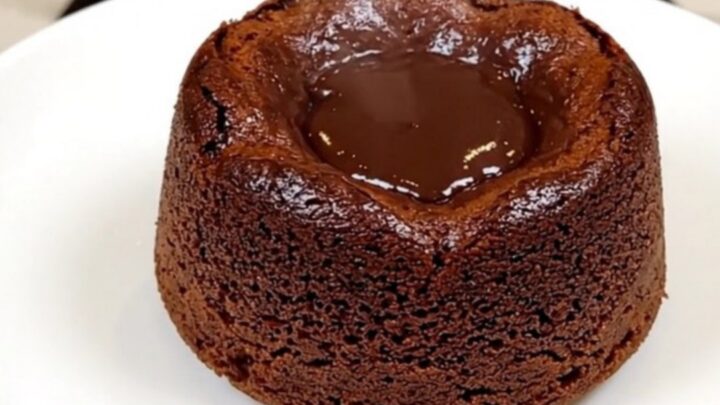 A top-down view of a black slow cooker filled with layers of chocolate cake mix, chips, and pudding before cooking.
