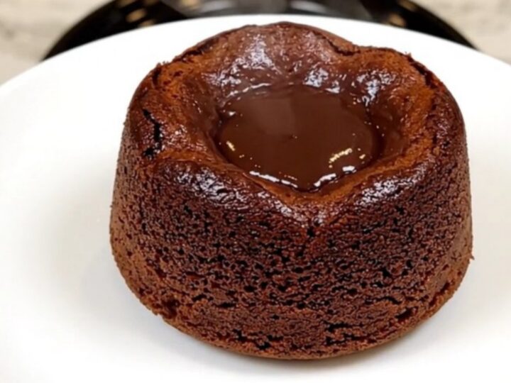 A top-down view of a black slow cooker filled with layers of chocolate cake mix, chips, and pudding before cooking.