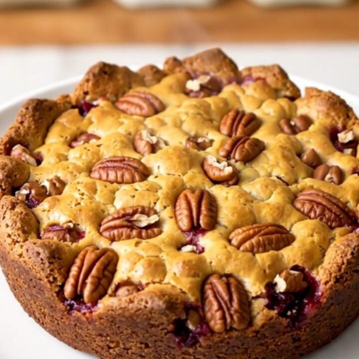 A warm, golden-brown pumpkin pecan cobbler served in a rustic slow cooker on a white quartz countertop.