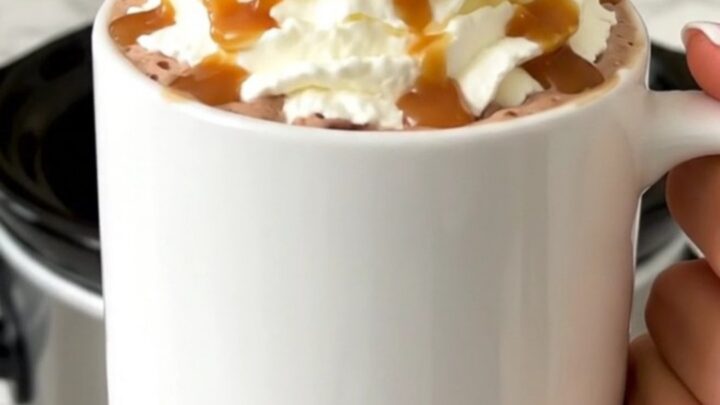 A steaming mug of salted caramel hot chocolate topped with whipped cream and caramel drizzle.