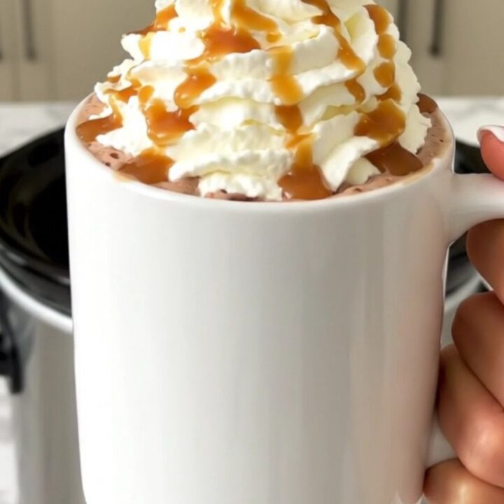 A steaming mug of salted caramel hot chocolate topped with whipped cream and caramel drizzle.