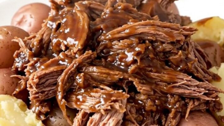 A hearty, rustic slow cooker pot roast served with tender red potatoes and a rich, dark glossy gravy on a white plate.