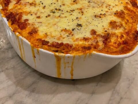 A deep, steaming slice of cheesy baked lasagna being lifted with a spatula, showing thick melted mozzarella cheese pulls.