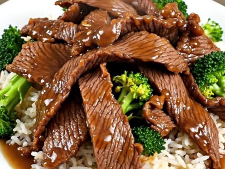 A white round plate featuring tender beef slices and bright green broccoli florets served over fluffy white rice.