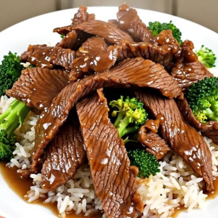 A white round plate featuring tender beef slices and bright green broccoli florets served over fluffy white rice.