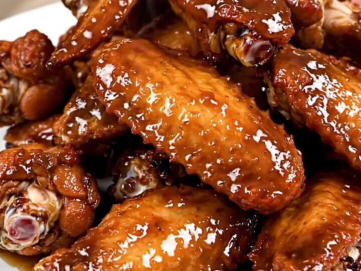 A close-up of glossy, caramelized chicken wings piled high on a white plate.
