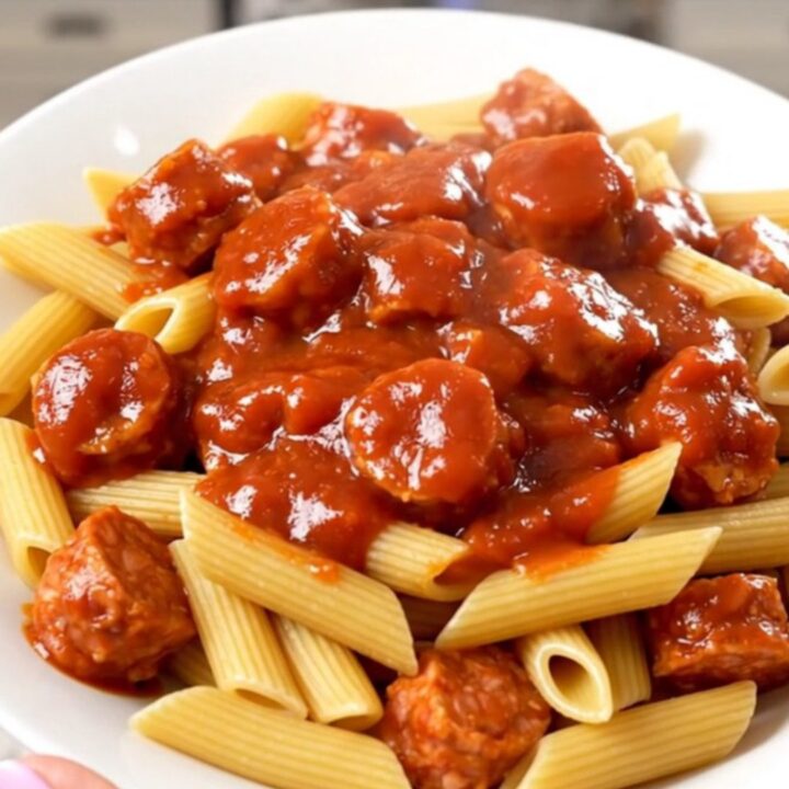 A steaming plate of penne pasta tossed in a rich marinara sauce with sliced Italian sausage and bell peppers.