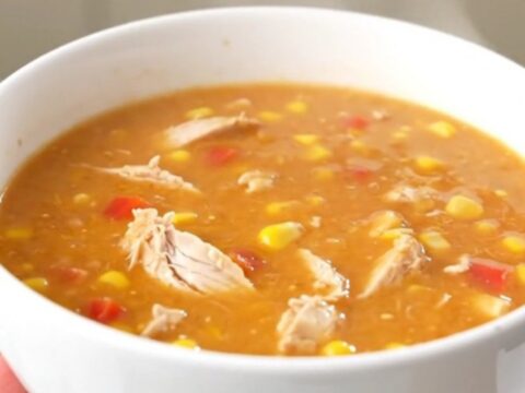 A steaming bowl of creamy buffalo chicken chowder with visible shredded chicken and corn.