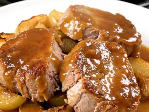 A close-up of sliced pork tenderloin with tender apples, topped with a glossy apple butter glaze on a white plate.