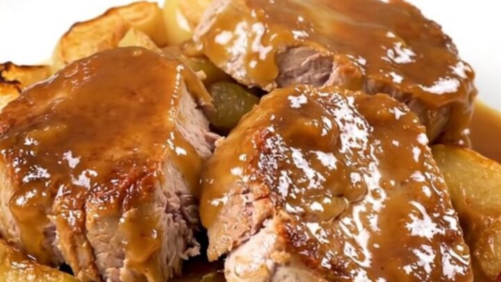 A close-up of sliced pork tenderloin with tender apples, topped with a glossy apple butter glaze on a white plate.