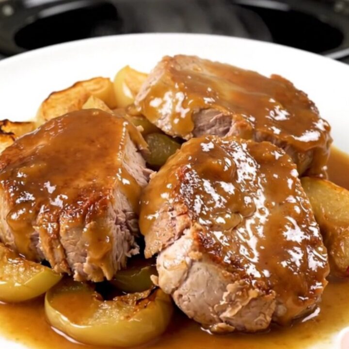 A close-up of sliced pork tenderloin with tender apples, topped with a glossy apple butter glaze on a white plate.