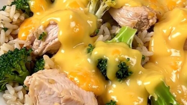 A slow cooker filled with chicken, broccoli, and a creamy cheddar sauce on a white speckled quartz countertop.