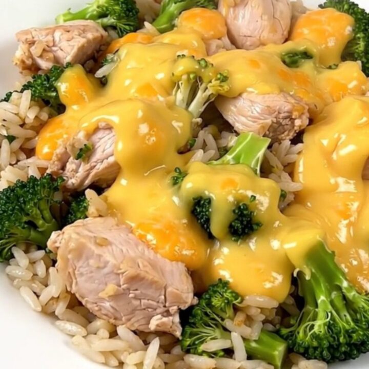 A slow cooker filled with chicken, broccoli, and a creamy cheddar sauce on a white speckled quartz countertop.