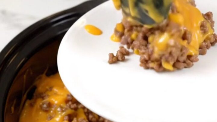 A steaming, cheesy beef and hash brown casserole in a black slow cooker on a white countertop.