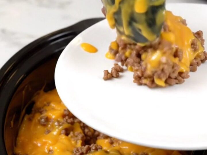 A steaming, cheesy beef and hash brown casserole in a black slow cooker on a white countertop.