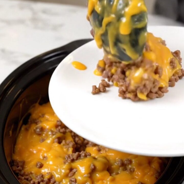 A steaming, cheesy beef and hash brown casserole in a black slow cooker on a white countertop.