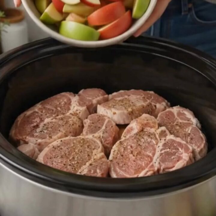 A fork cutting through a juicy, glazed slow cooker pork chop topped with caramelized apple wedges and rich jus