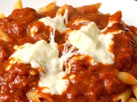 A top-down view of a slow cooker filled with meatballs, penne pasta, and marinara sauce.