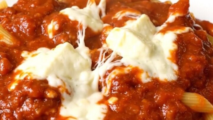 A top-down view of a slow cooker filled with meatballs, penne pasta, and marinara sauce.