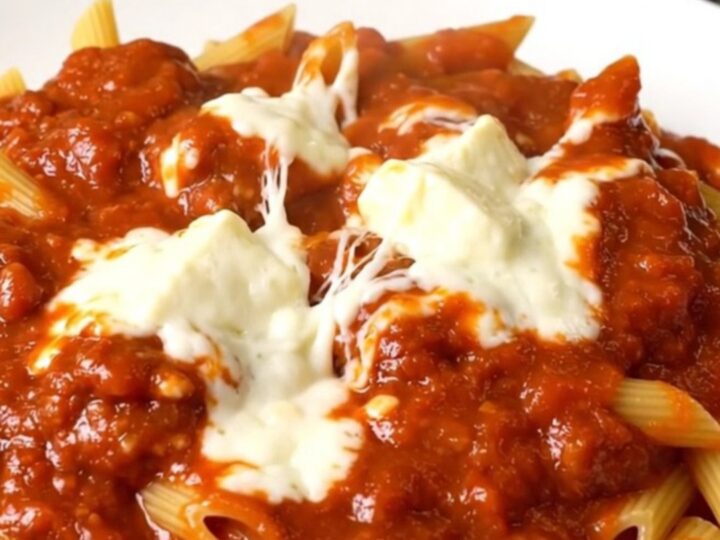 A top-down view of a slow cooker filled with meatballs, penne pasta, and marinara sauce.