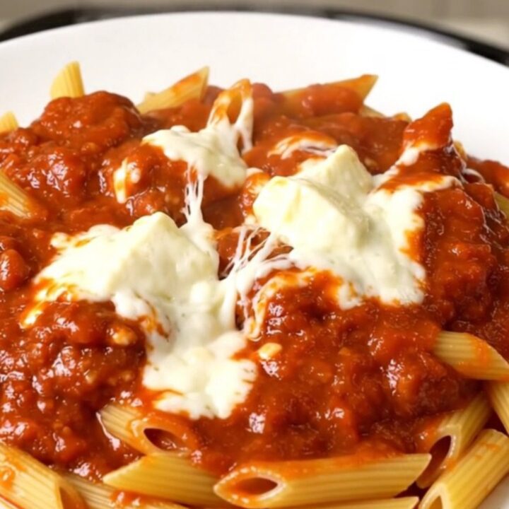 A top-down view of a slow cooker filled with meatballs, penne pasta, and marinara sauce.