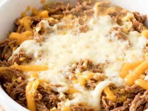 A creamy Philly cheesesteak dip in a white bowl with melted cheese and beef.