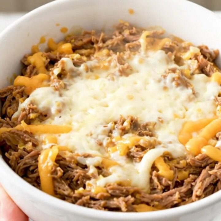 A creamy Philly cheesesteak dip in a white bowl with melted cheese and beef.