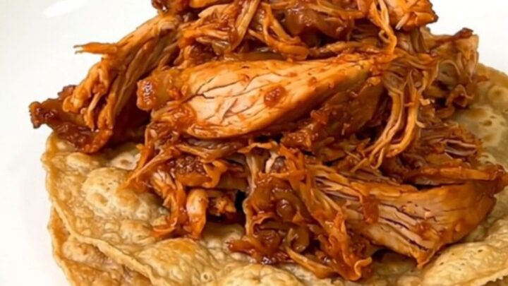 A close-up shot of steaming shredded chicken tinga piled high on crisp tostadas on a white plate.