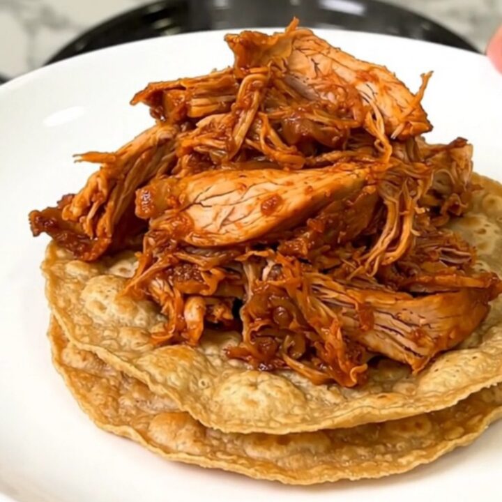 A close-up shot of steaming shredded chicken tinga piled high on crisp tostadas on a white plate.