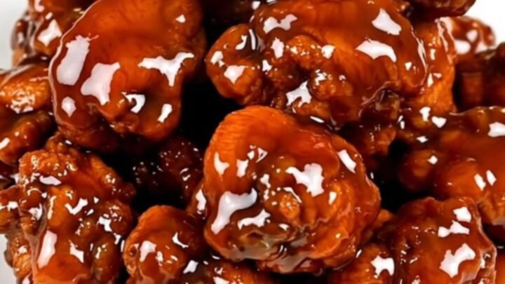 A close-up of glossy General Tso chicken on a white plate, steaming slightly.