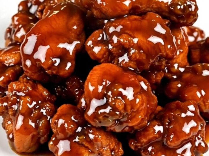 A close-up of glossy General Tso chicken on a white plate, steaming slightly.