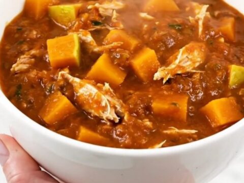 A white ceramic bowl filled with steaming turkey and butternut squash chili on a table.