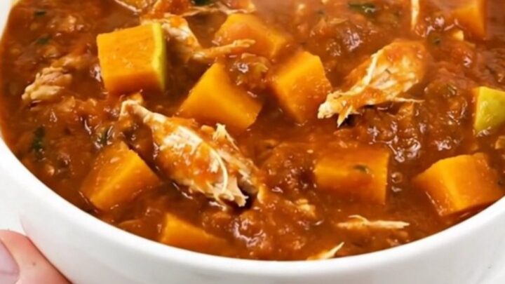 A white ceramic bowl filled with steaming turkey and butternut squash chili on a table.