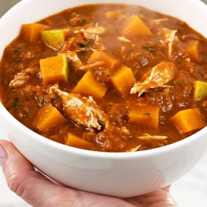 A white ceramic bowl filled with steaming turkey and butternut squash chili on a table.