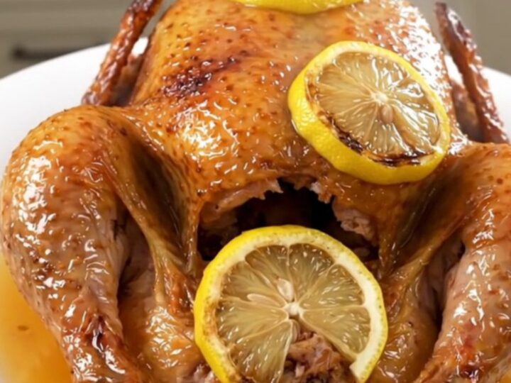 A slow cooker filled with a whole raw chicken, lemon slices, and garlic, ready to be cooked.