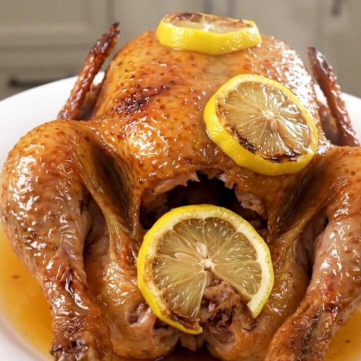 A slow cooker filled with a whole raw chicken, lemon slices, and garlic, ready to be cooked.