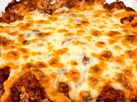 A steaming beef enchilada casserole in a black slow cooker on a white speckled countertop.
