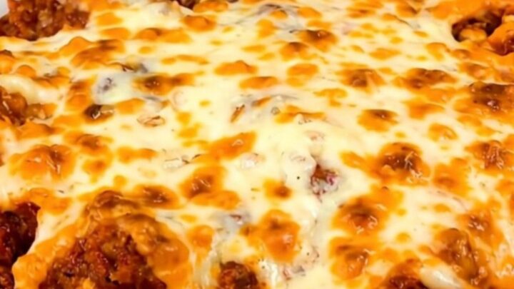 A steaming beef enchilada casserole in a black slow cooker on a white speckled countertop.